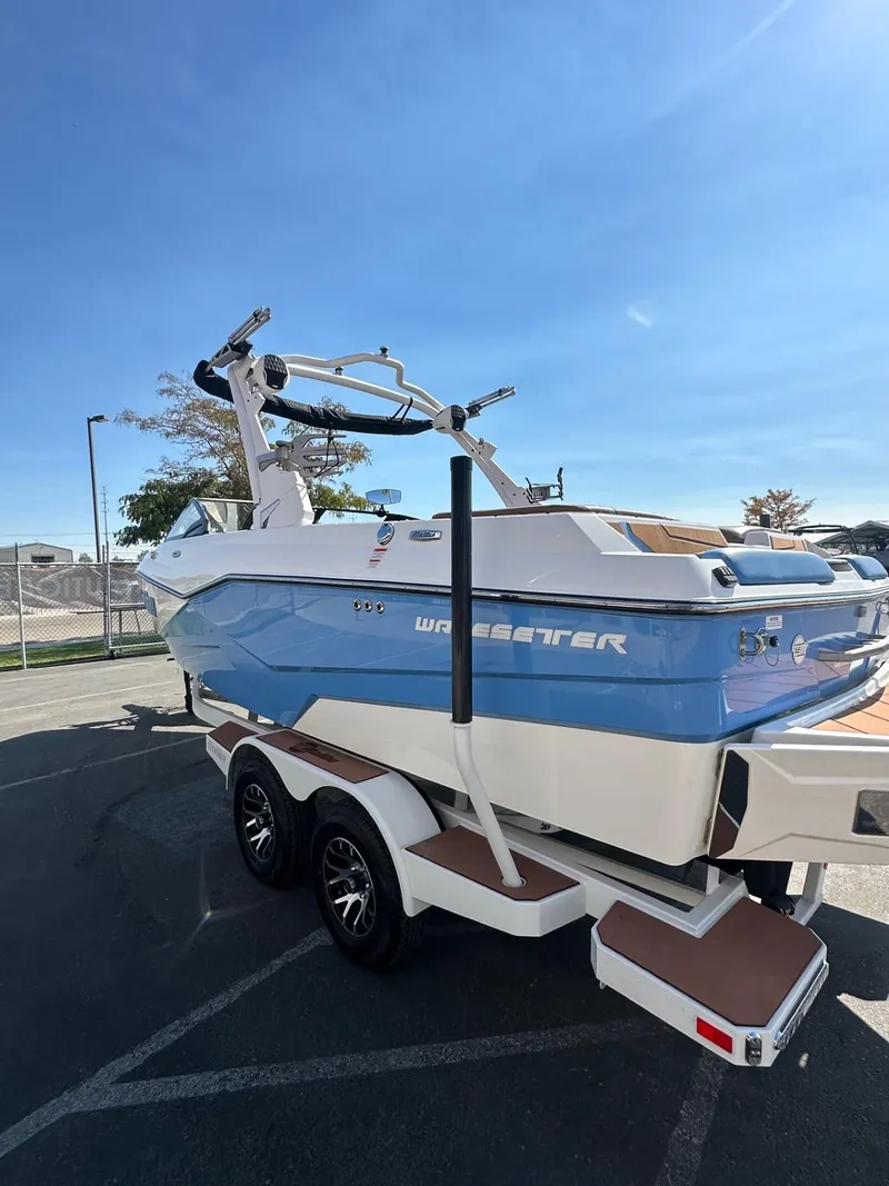 Slide: The Image of 2024 Malibu 22 LSV Wakesetter boat on trailer, blue and white design, sunny day. - 7