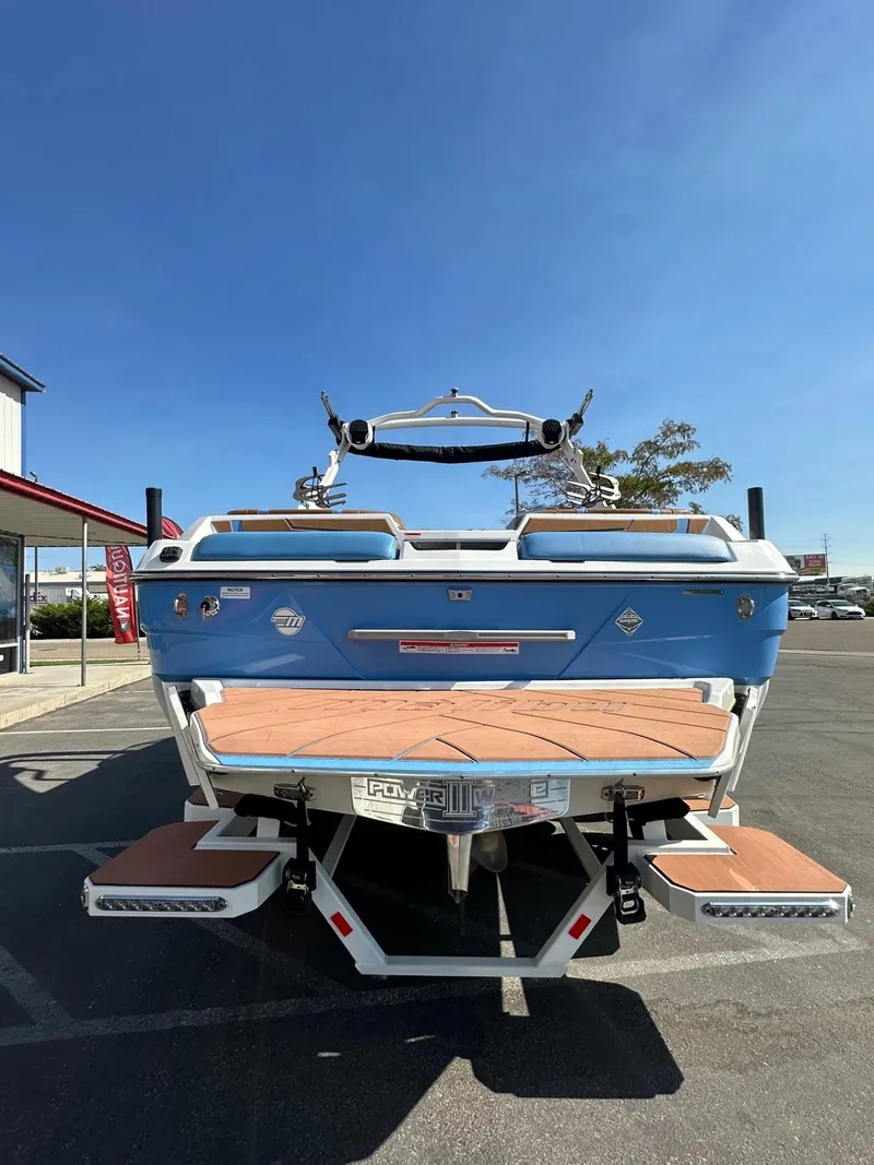 Slide: The Image of 2024 Malibu 22 LSV boat, blue exterior, parked outdoors under clear sky. - 8