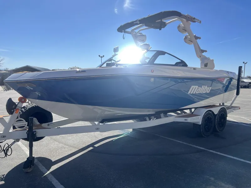 Slide: The Image of 2024 Malibu 23 LSV boat on trailer, blue and white design, sunny day. - 5