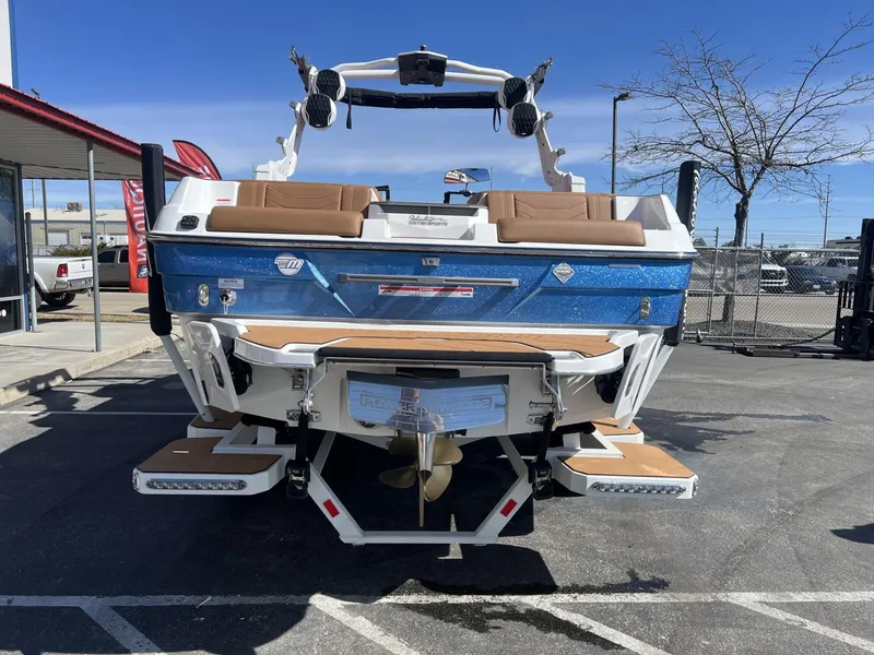 Slide: The Image of 2024 Malibu 23 LSV boat, blue exterior, parked outdoors, showcasing rear view and swim platform. - 8