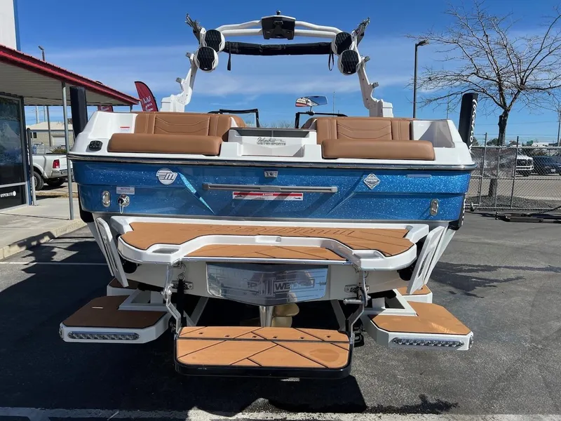 Slide: The Image of 2024 Malibu 23 LSV boat with blue exterior and tan seating, parked outdoors. - 9
