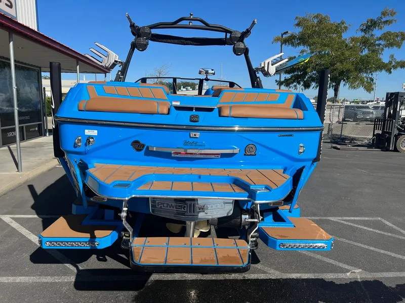 Slide: The Image of 2024 Malibu 24 MXZ boat, blue exterior, parked outdoors, showcasing rear deck and seating. - 10