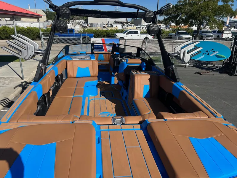 Slide: The Image of 2024 Malibu 24 MXZ boat interior with brown and blue seating, docked outdoors. - 11