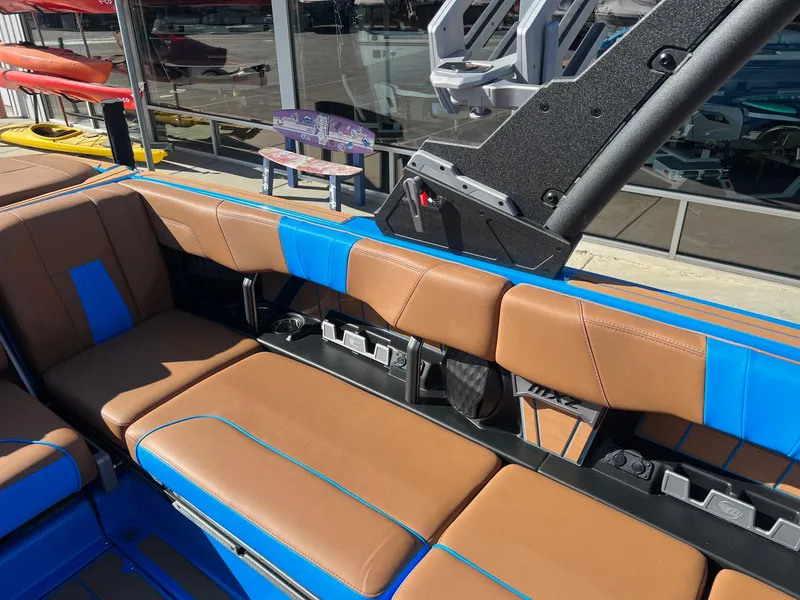 Slide: The Image of 2024 Malibu 24 MXZ boat interior with brown and blue seating, docked near kayaks. - 13