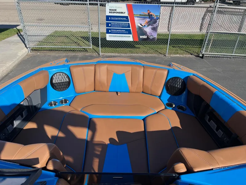 Slide: The Image of 2024 Malibu 24 MXZ boat interior with blue and brown seating, docked near a safety sign. - 19