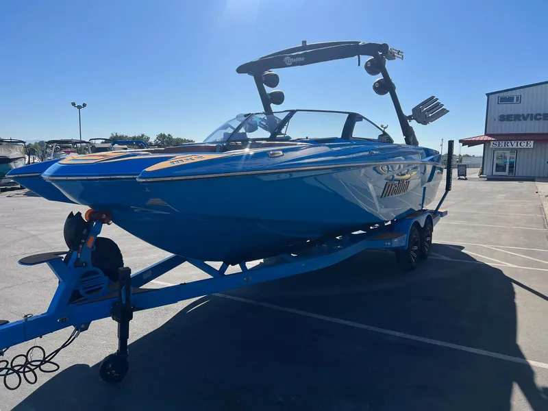 Slide: The Image of 2024 Malibu 24 MXZ boat in vibrant blue on a trailer, parked near a service building. - 5