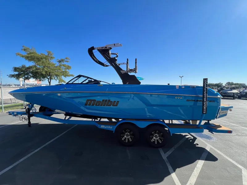 Slide: The Image of 2024 Malibu 24 MXZ boat in vibrant blue on a trailer, parked outdoors. - 6