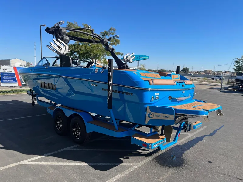 Slide: The Image of 2024 Malibu 24 MXZ boat in vibrant blue, parked on a trailer in a sunny lot. - 7