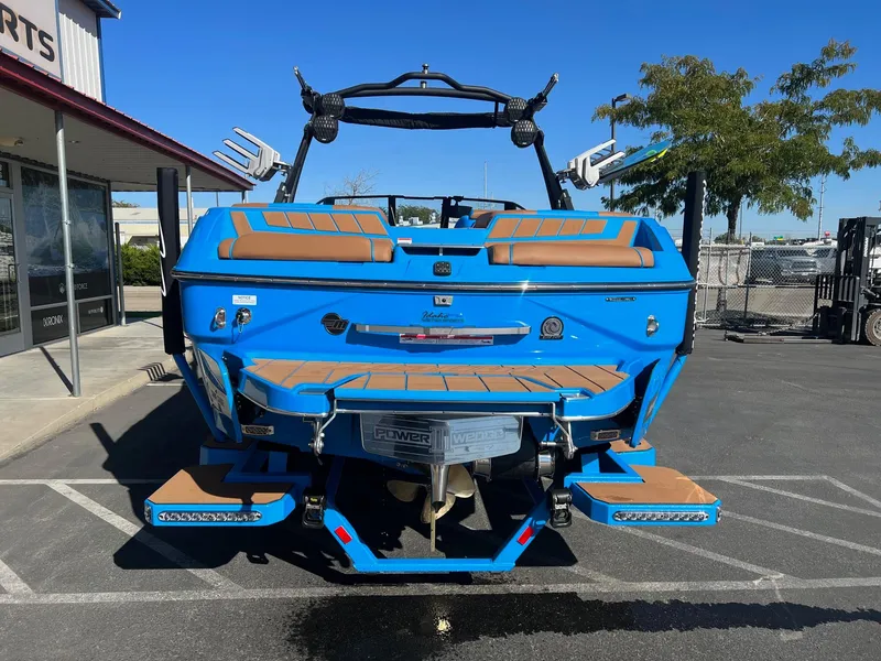 Slide: The Image of 2024 Malibu 24 MXZ boat, blue exterior, parked outdoors, rear view. - 8