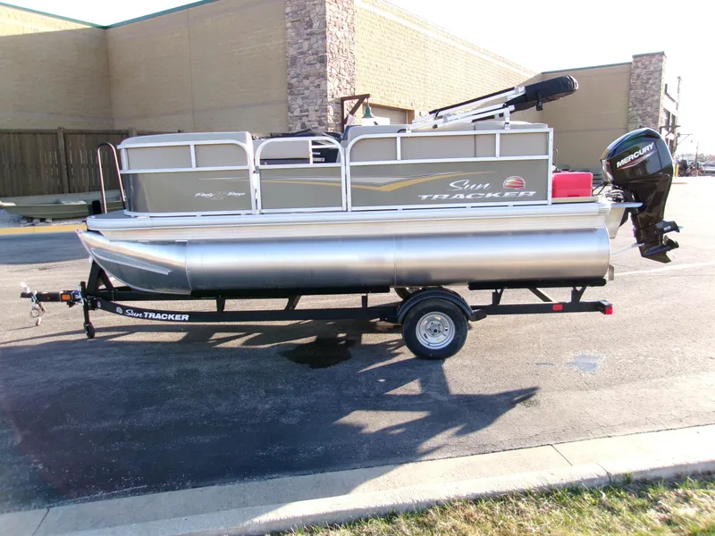 Slide: The Image of 2025 Sun Tracker Party Barge 16 DLX pontoon boat on trailer, parked outdoors. - 2