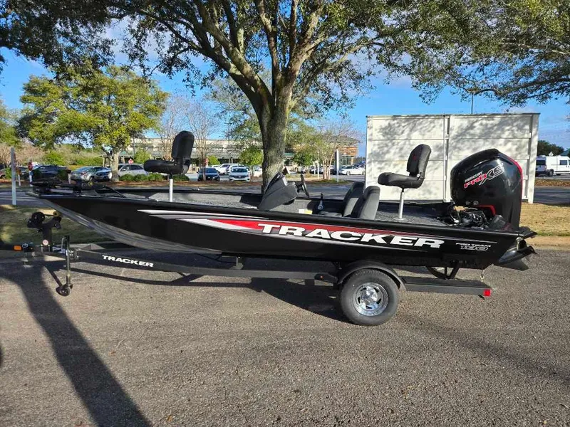 Slide: The Image of 2025 Tracker Pro Team 190 boat on trailer, parked outdoors under trees. - 2