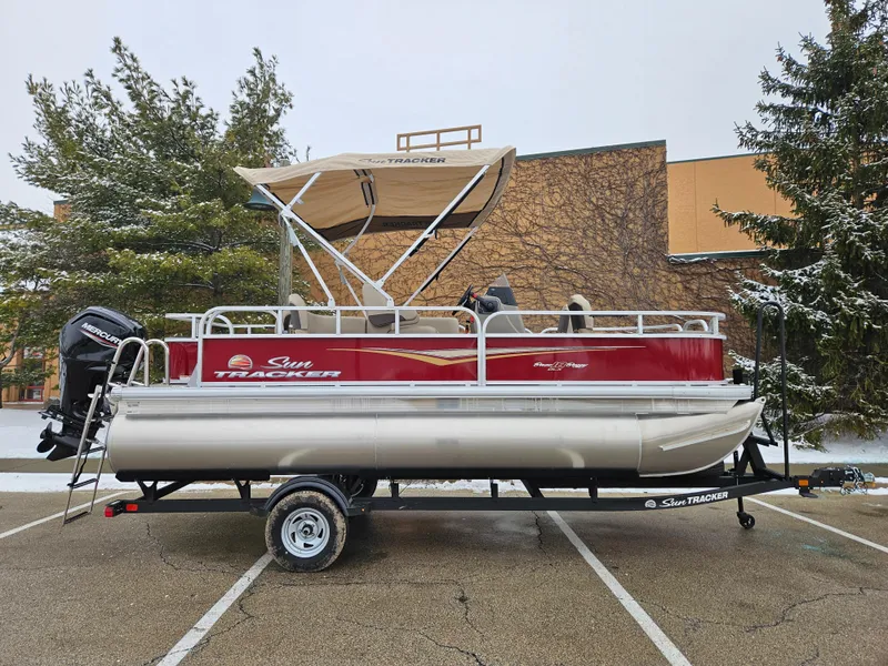 The Image of 2025 Sun Tracker Bass Buggy 18 DLX pontoon boat on trailer in parking lot. - 0