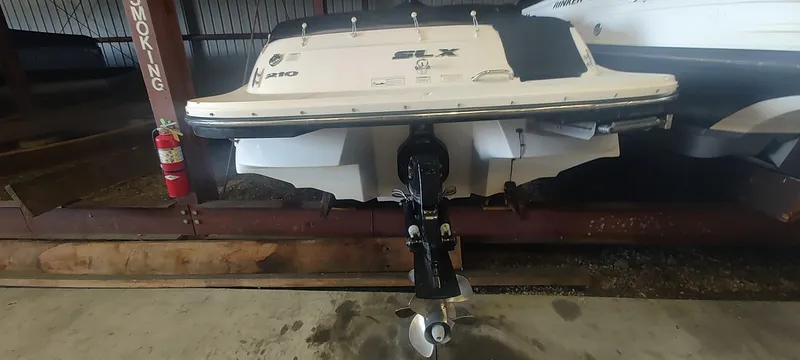 Slide: The Image of 2013 Sea Ray 210 SLX boat stored indoors, rear view with visible outboard motor. - 21