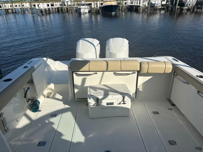 Slide: The Image of 2020 Pursuit DC 295 Dual Console boat interior with seating and cooler, docked by the water. - 12