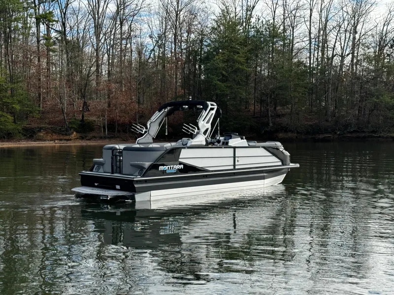 Slide: The Image of 2025 Montara Surf Boss 2.0 25 pontoon boat on a calm lake, surrounded by trees. - 9