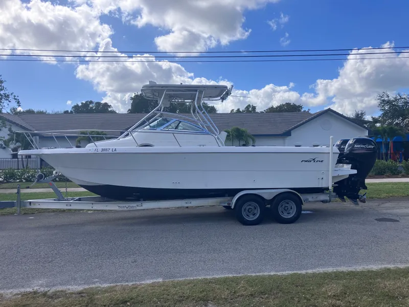 The Image of 1998 Pro-Line 241 Walkaround boat on trailer, parked on street, under a partly cloudy sky. - 0