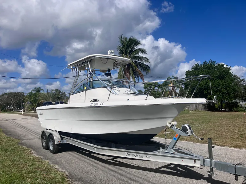 Slide: The Image of 1998 Pro-Line 241 Walkaround boat on trailer, parked on a sunny street with palm trees. - 3