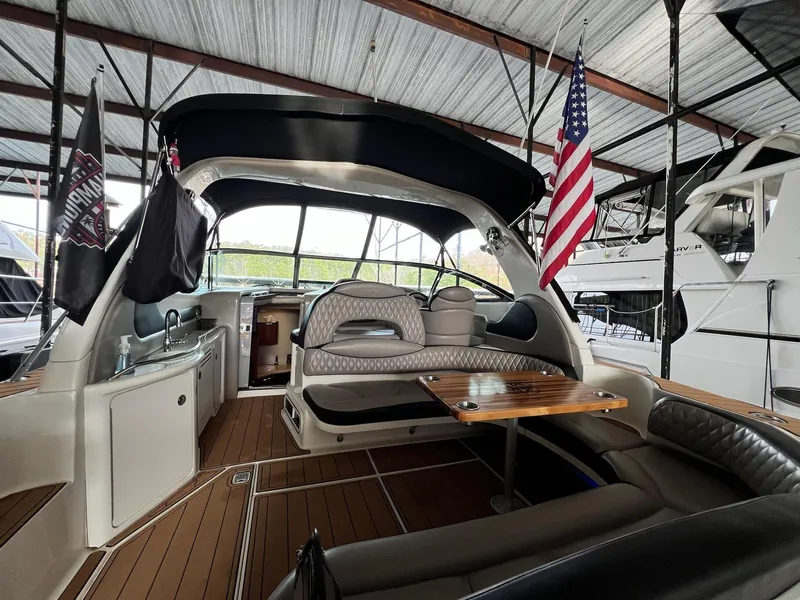 Slide: The Image of 2002 Sea Ray 380 Sundancer interior with seating, table, and American flag in a marina. - 24