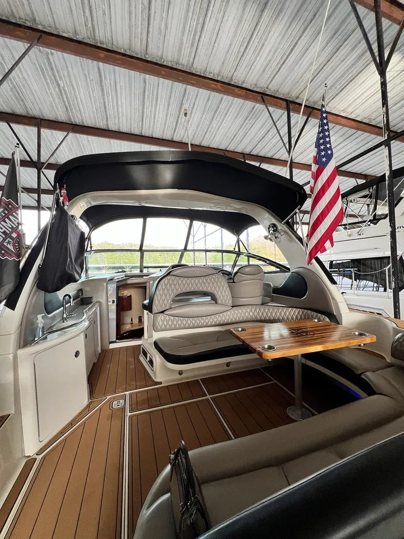 Slide: The Image of 2002 Sea Ray 380 Sundancer interior with seating, table, and American flag under a covered dock. - 25