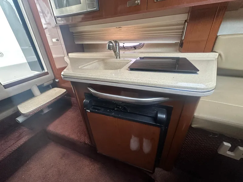 Slide: The Image of 2012 Sea Ray 280 Sundancer interior kitchen with sink, stove, and compact fridge. - 17