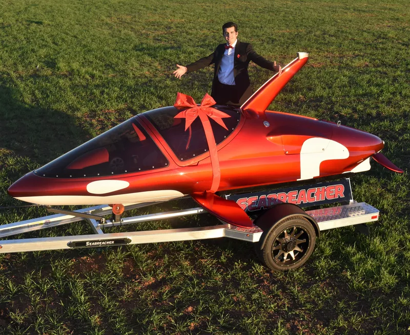 Slide: The Image of 2025 Seabreacher X, Y, Z with red bow on trailer, man standing beside it. - 19