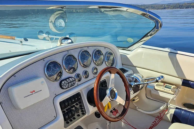 Slide: The Image of 2006 Chris-Craft Corsair 28 dashboard with gauges and wooden steering wheel on calm water. - 38