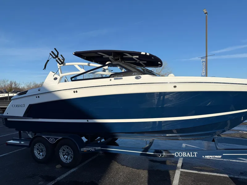 Slide: The Image of 2025 Cobalt R6 Surf boat on trailer, blue and white design, parked outdoors. - 48