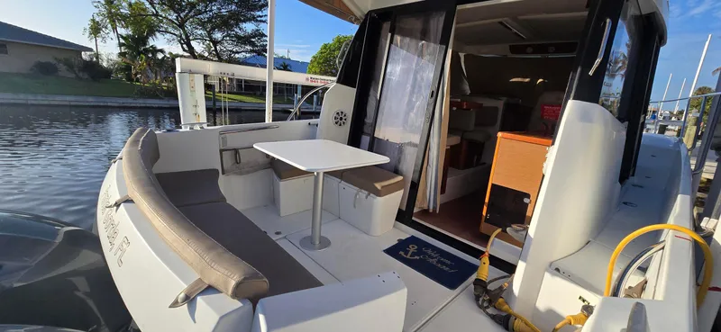 Slide: The Image of 2016 Jeanneau Merry Fisher 855 boat with outdoor seating and table, docked by the water. - 7