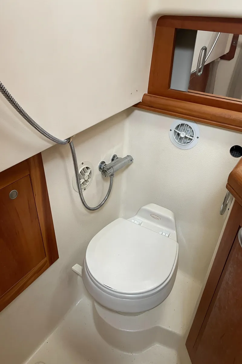 Slide: The Image of 2006 Mainship Pilot 34 boat bathroom with toilet, showerhead, and wooden cabinetry. - 18