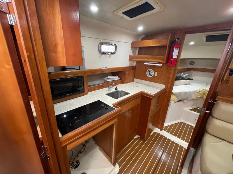 Slide: The Image of 2006 Mainship Pilot 34 interior with kitchenette, wood cabinetry, and cozy seating area. - 27