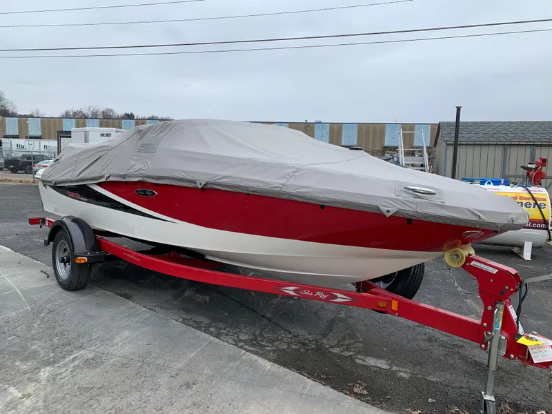 Slide: The Image of 2013 Sea Ray 190 Sport boat, red and white, covered, on a trailer in a parking lot. - 9
