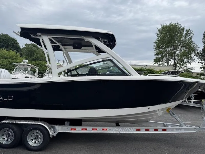 Slide: The Image of 2025 Robalo R 257 boat on trailer, sleek black and white design, parked outdoors. - 2