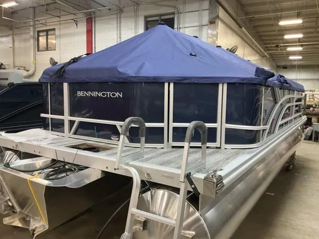 Slide: The Image of 2025 Bennington S L-Bench 21 SLJ pontoon boat with blue cover in a warehouse. - 14