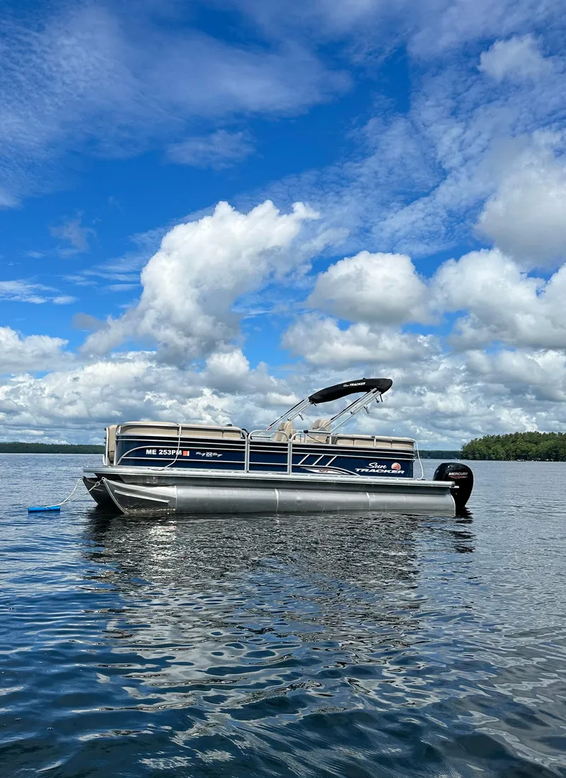 The Image of 2022 Sun Tracker PB 22 XP3 pontoon boat on a serene lake under a blue sky. - 1
