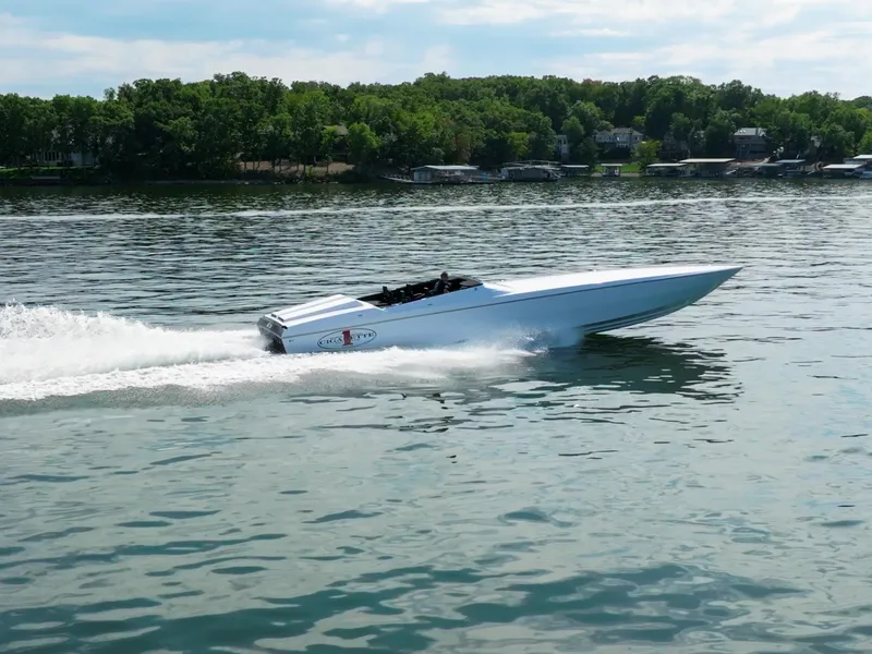 The Image of 2023 Cigarette 515 speedboat cruising on a lake with lush green shoreline. - 2