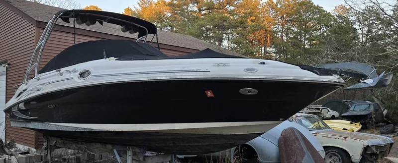 Slide: The Image of 2006 Sea Ray 270 Sundeck boat on dry dock, surrounded by trees and vintage cars. - 2