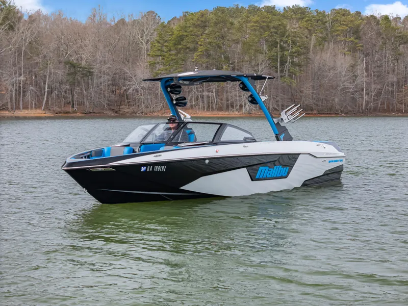 Slide: The Image of 2021 Malibu Wakesetter 25 LSV boat on a lake with forested background. - 2