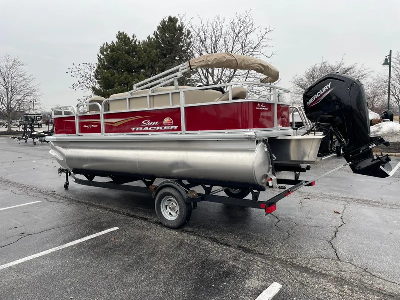 Slide: The Image of 2025 Sun Tracker Bass Buggy 18 DLX pontoon boat on trailer in parking lot. - 2