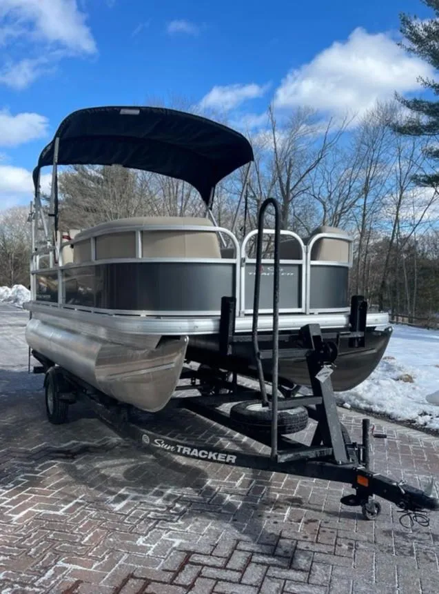 Slide: The Image of 2025 Sun Tracker Party Barge 16 DLX pontoon boat on trailer, parked on snowy driveway. - 2