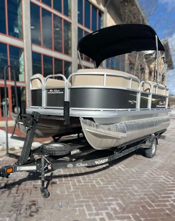 Slide: The Image of 2025 Sun Tracker Party Barge 16 DLX pontoon boat on a trailer, parked outdoors. - 3