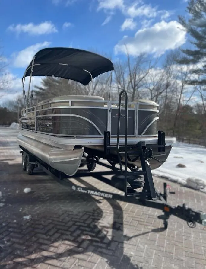 Slide: The Image of 2025 Sun Tracker Party Barge 22 DLX pontoon boat on trailer, parked on snowy driveway. - 2