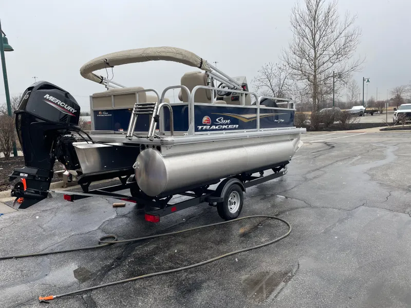 Slide: The Image of 2025 Sun Tracker Bass Buggy 16 XL Select pontoon boat on trailer, parked outdoors. - 3