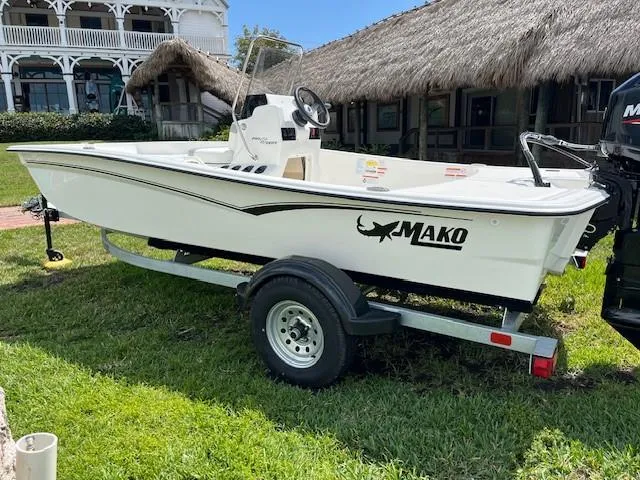Slide: The Image of 2025 Mako Pro Skiff 15 CC with Mercury 60 engine on grass near thatched building. - 2