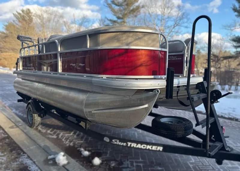 Slide: The Image of 2025 Sun Tracker Party Barge 18 DLX pontoon boat on trailer, parked outdoors. - 2