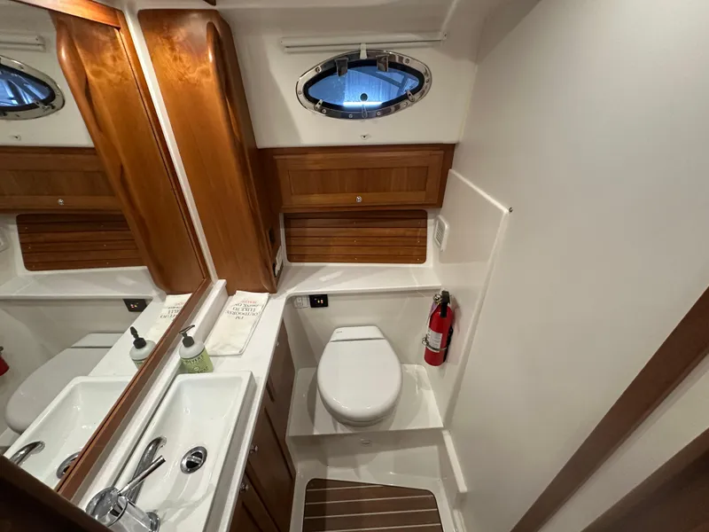 Slide: The Image of 2018 Back Cove 32 yacht bathroom with wooden accents, mirror, sink, and porthole window. - 13
