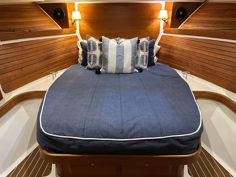 Slide: The Image of 2018 Back Cove 32 cabin interior with cozy bed, wooden paneling, and decorative pillows. - 16