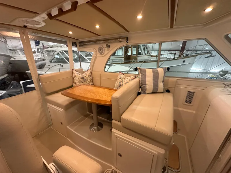 Slide: The Image of 2018 Back Cove 32 interior with beige seating and wooden table in a marina setting. - 9
