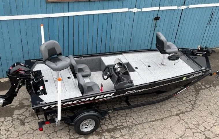 Slide: The Image of 2024 Tracker Pro 170 fishing boat with gray seating, parked on a trailer by a blue wall. - 6