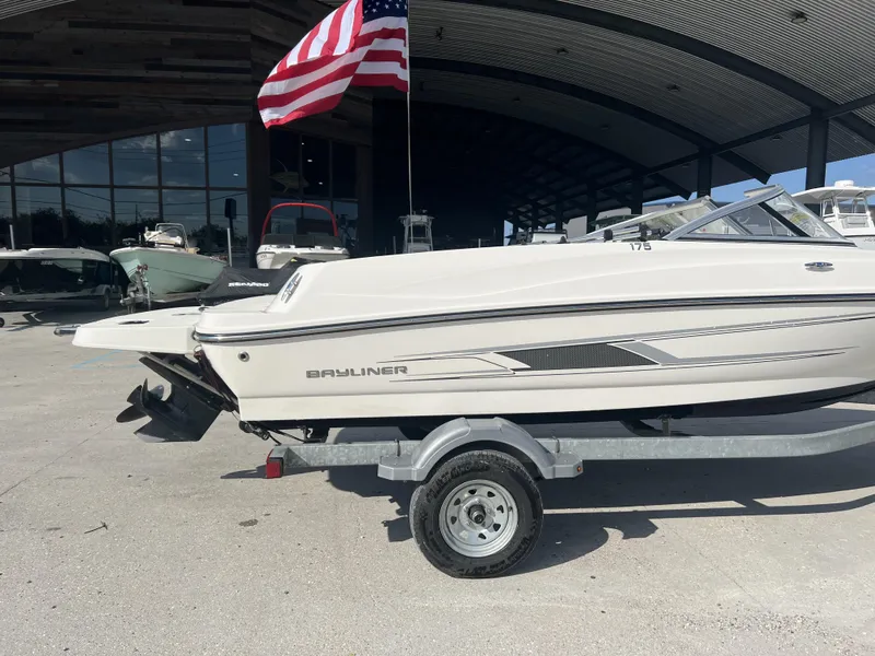 Slide: The Image of 2016 Bayliner 175 boat on trailer, parked outdoors with American flag above. - 13