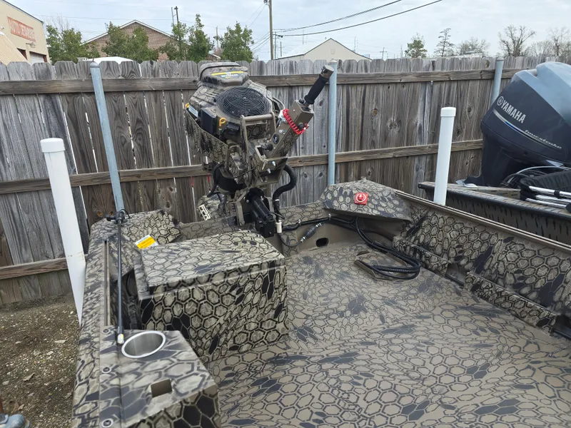 Slide: The Image of 2025 Pro-Drive 1848 SBX boat with camouflage pattern and outboard motor, parked by a wooden fence. - 4